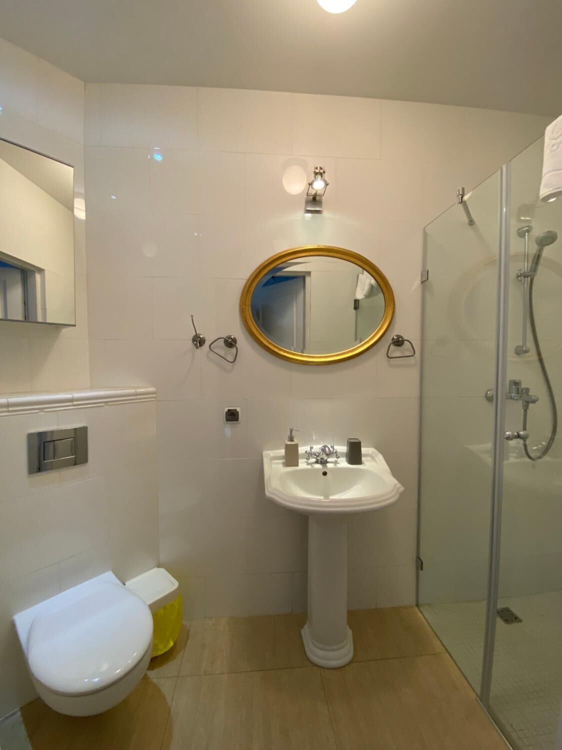 A bathroom with a white toilet, a pedestal sink, a mirror with a gold frame, and a glass-enclosed shower.