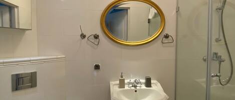 A bathroom with a white toilet, a pedestal sink, a mirror with a gold frame, and a glass-enclosed shower.