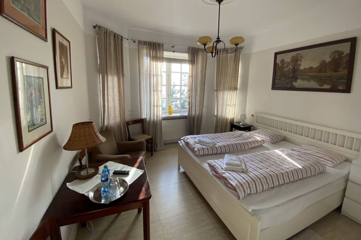 A hotel room with a bed, bedside tables, a desk with a lamp, a chair, and curtains.