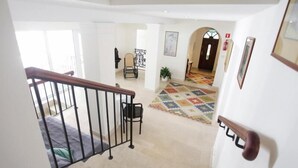 A spacious hallway with a wooden staircase, a patterned rug, and a door with a handle.