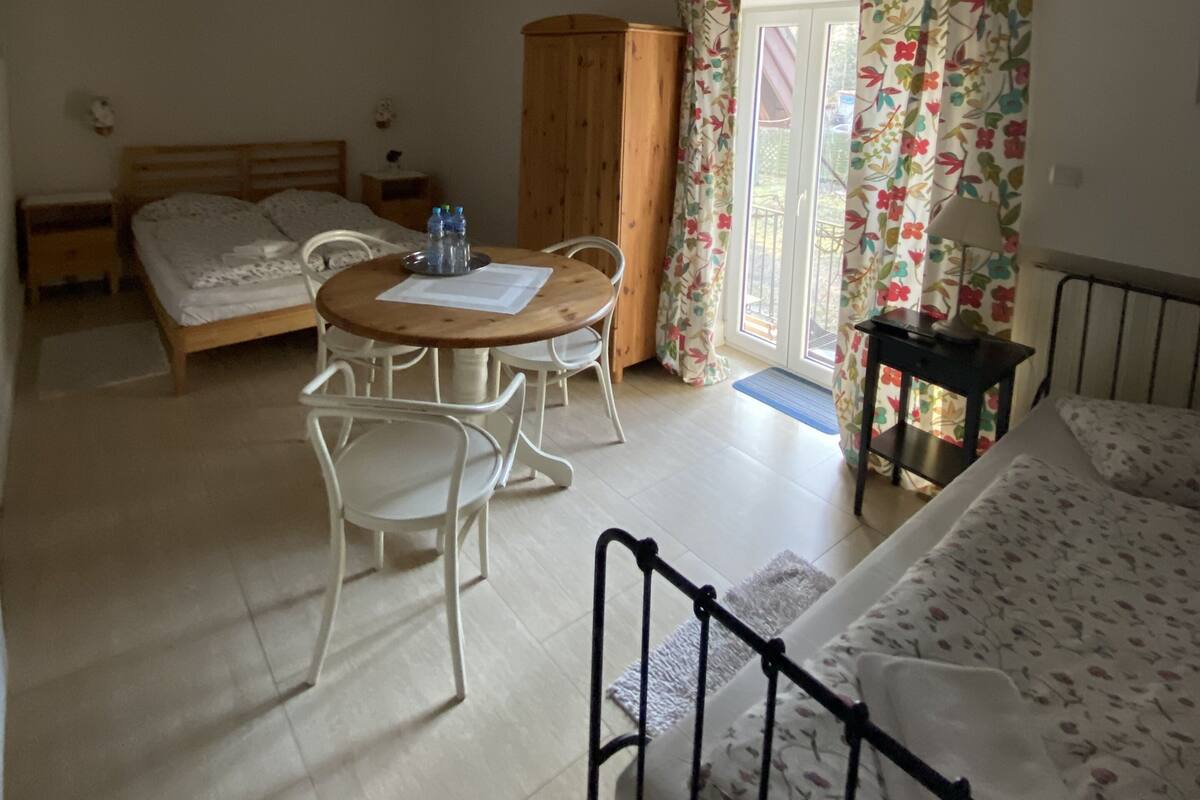 A bedroom with a bed, a desk with chairs, a wardrobe, and a window with curtains.