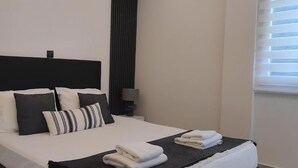 A neatly made bed with a black headboard, white and striped pillows, and folded towels on a dark bedspread. - Inas Διαμέρισμα 2 υπνοδωματίων (Lefkimmi)
