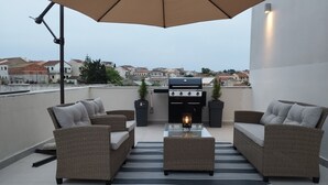 A rooftop patio with wicker furniture, a grill, and a view of the cityscape. - Inas Διαμέρισμα 2 υπνοδωματίων (Lefkimmi)