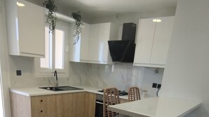 A modern kitchen with white cabinets, a black range hood, and a dining area with bar stools. - Inas Διαμέρισμα 2 υπνοδωματίων (Lefkimmi)