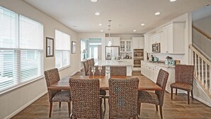 A spacious kitchen with white cabinets, a central island, and a dining area with patterned chairs.