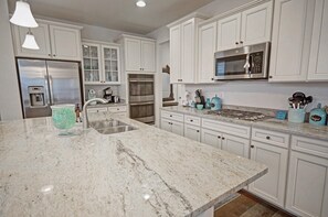 Une cuisine moderne avec des meubles blancs, des appareils en acier inoxydable et un plan de travail en granit.