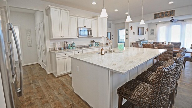 A spacious kitchen with white cabinets, a large island, and bar stools.