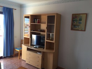 Un salon avec un meuble de rangement en bois, un téléviseur et un fauteuil.