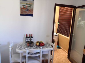 Une table à manger recouverte d’une nappe à motifs, avec deux bouteilles de vin et un saladier rempli de fruits.