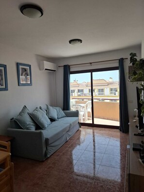 Un salon avec un canapé, un téléviseur et un balcon donnant sur des immeubles.