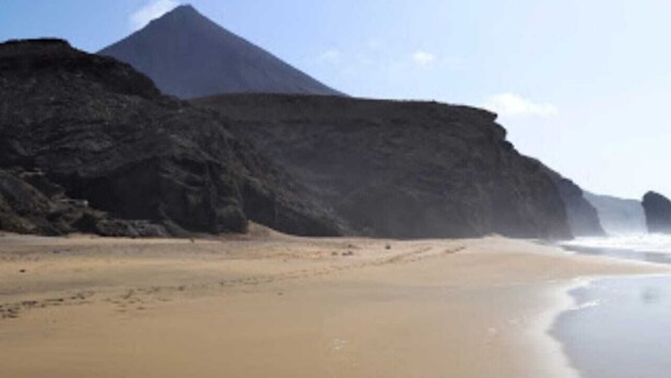 A beach with a large rock formation in the background and a clear sky.