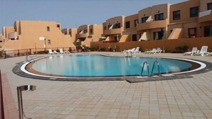 A swimming pool with lounge chairs and a tiled deck, surrounded by buildings with balconies.