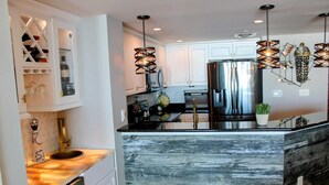 A modern kitchen with a central island, stainless steel appliances, and pendant lighting. - MVG 909 Oceanfront NEW UPDATES (North Myrtle Beach)