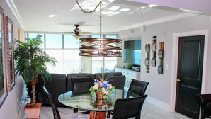 A dining area with a glass table surrounded by chairs, a ceiling fan, and a potted plant. - MVG 909 Oceanfront NEW UPDATES (North Myrtle Beach)