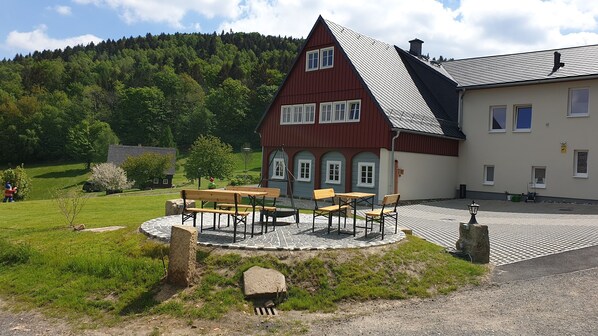 A traditional house with a red roof and white walls, a paved courtyard with a wooden table and chairs, and a stone well.