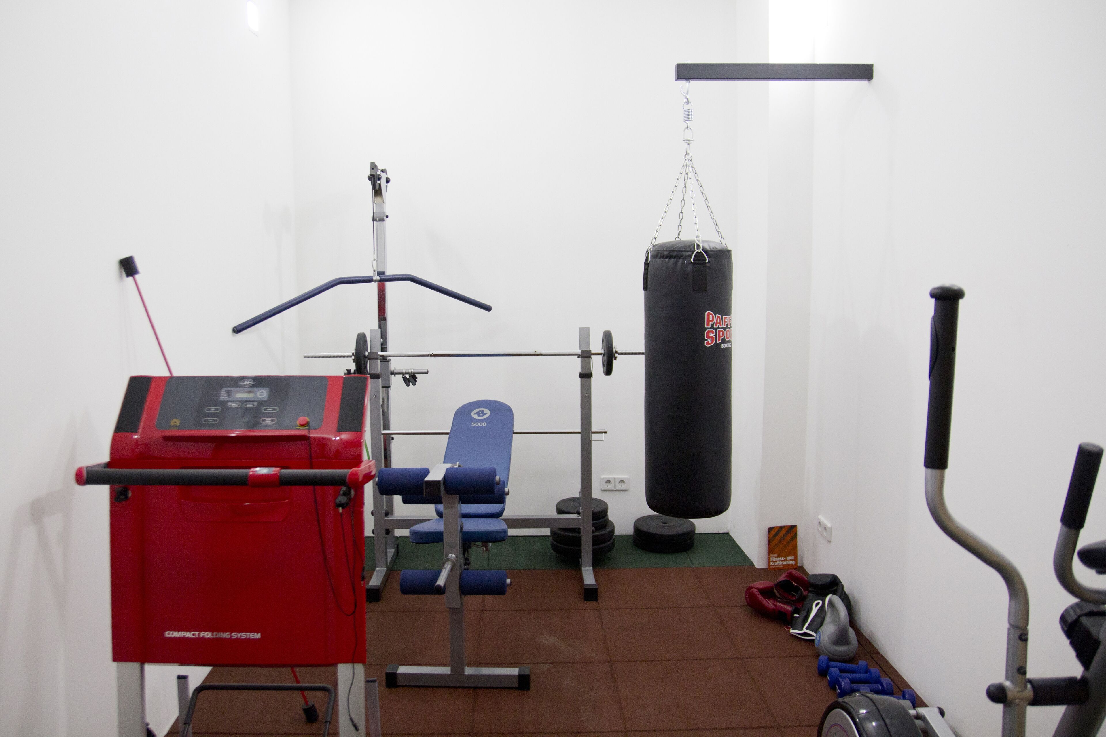 A gym with a compact folding system, a punching bag, a bench, and an exercise bike.