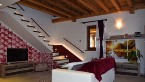 A living room with a white sofa, a TV, a staircase, and a wall with a painting. - Cadorna Residence in Sonia (Tarvisio)