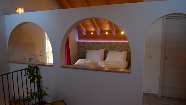 A bedroom with a bed under a wooden ceiling, two arched windows, and a small plant. - Cadorna Residence in Sonia (Tarvisio)