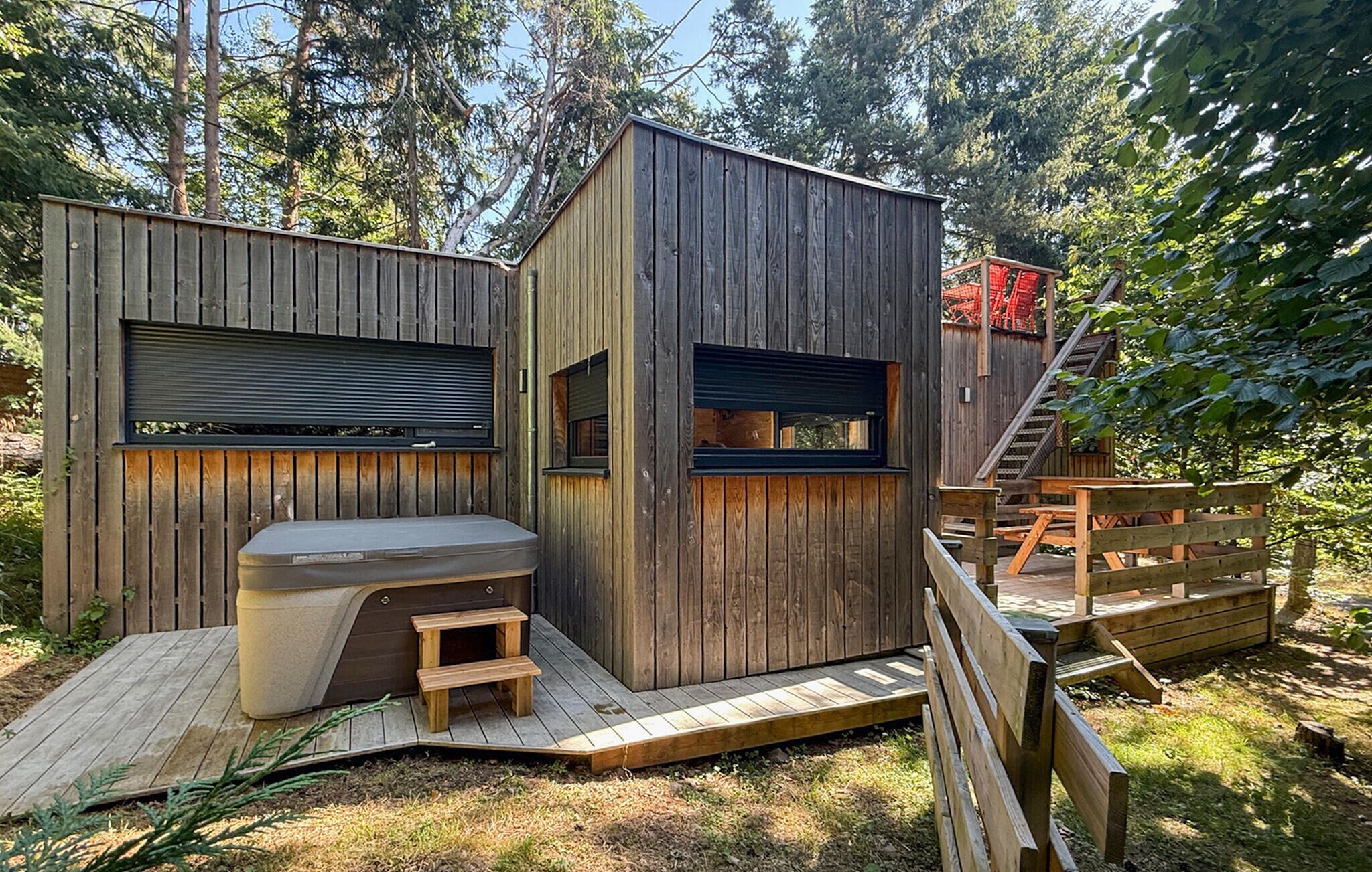 Une cabane en bois dotée d’un jacuzzi intégré, d’une petite terrasse et d’un escalier menant à une mezzanine.
