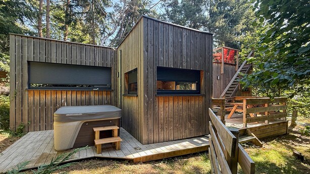 Eine Holzhütte mit eingebautem Whirlpool, einer kleinen Terrasse und einer Treppe, die zu einem Schlafbereich im oberen Geschoss führt.