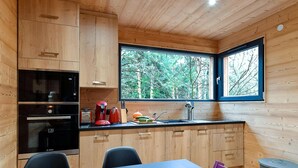 Eine kleine Küche mit Holdekor, einem Bosch-Ofen, einer roten Kaffeemaschine und einem Fenster mit Blick auf einen Wald.