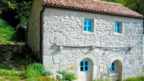 A stone building with a tiled roof, two windows with blue frames, and a small arched entrance. - Authentic stone built villetta with a magnificent view (Grižane)