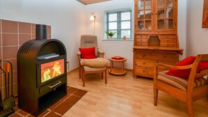 A cozy living room with a wood-burning stove, two chairs, a wooden cabinet, and a window with blinds. - 3 bedroom cozy home in Sydals (Sydals)