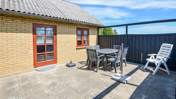 A patio with a table and chairs, a wooden fence, and a brick building with red-framed windows. - 3 bedroom cozy home in Sydals (Sydals)