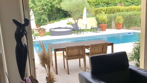 A living room with a black leather sofa, a dining table with chairs, and a view of a swimming pool and garden. - Villa with a heated pool and a lazy river, incredible views of the mountains (Tourrettes-sur-Loup)