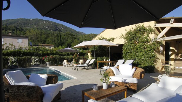 A poolside area with wicker furniture, white cushions, and umbrellas. - Villa with a heated pool and a lazy river, incredible views of the mountains (Tourrettes-sur-Loup)