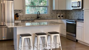A modern kitchen with white cabinetry, a granite countertop, a built-in microwave, a stainless steel refrigerator, and a large window with a view of trees. - Wildwood on the lake, views, private dock, quiet cove, dog friendly  (Gainesville)