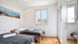 Une chambre avec deux lits, une grande fenêtre donnant sur la ville et un tableau accroché au mur.
