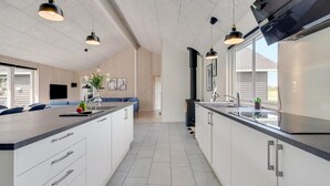 Ett modernt kök med en central köksö, hängande lampor och ett stort fönster.