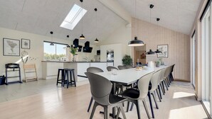Ett rymligt kök med en central köksö, modern hängande belysning och utsikt över utomhusmiljön.