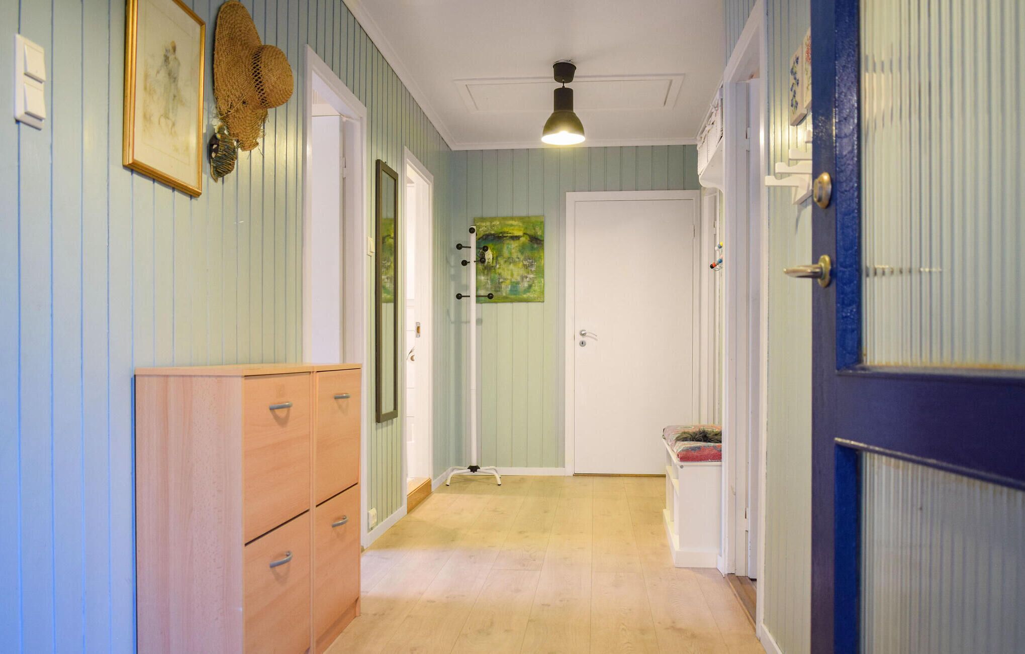 A hallway with light blue walls, a wooden dresser, a ceiling fan, and a door with a blue frame.