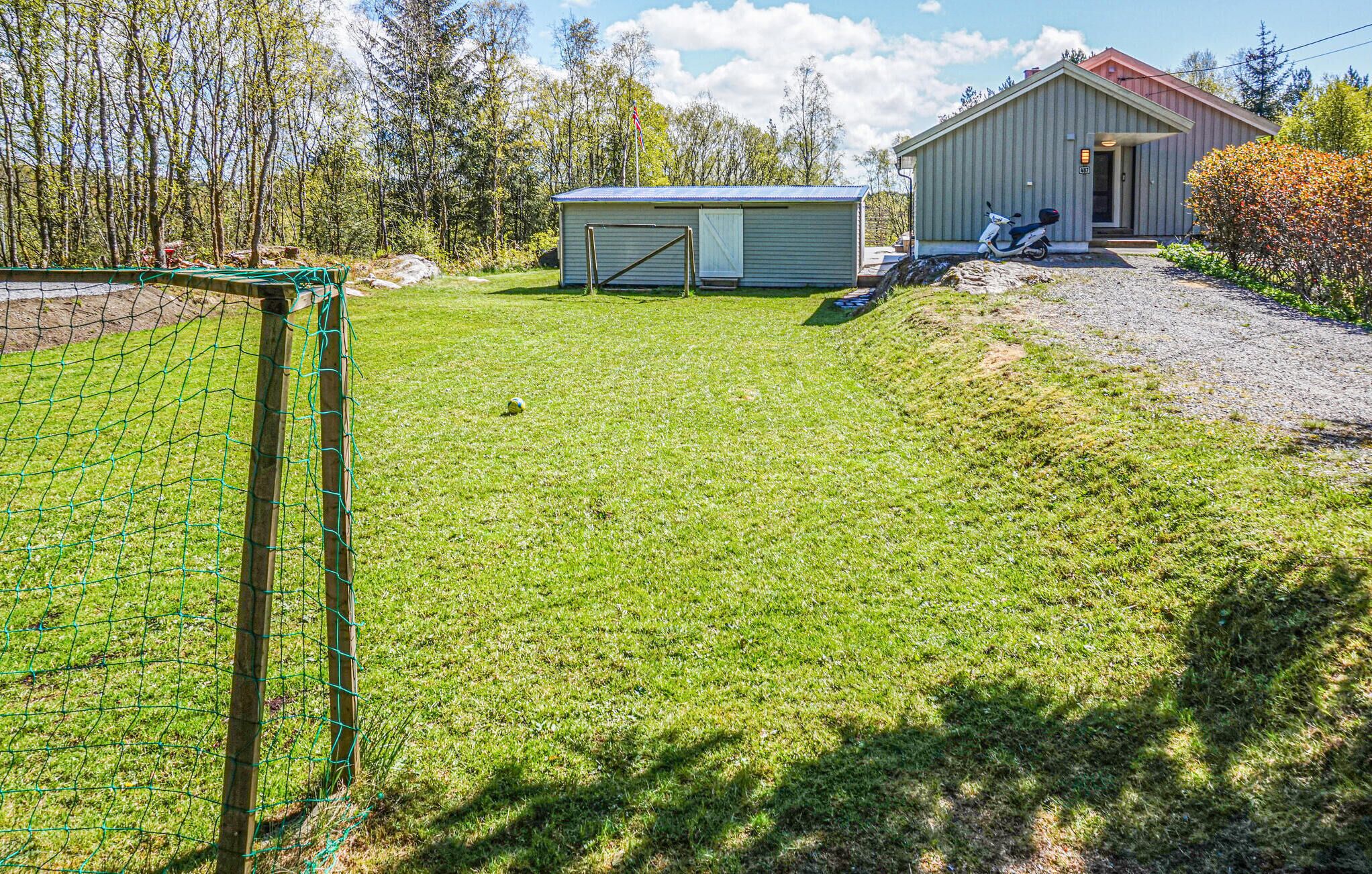 Ein umzäunter Garten mit einem kleinen Schuppen, einem Roller und einem Haus im Hintergrund.