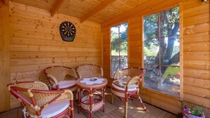 A wooden cabin with a dartboard, wicker chairs, a small table, and a large window offering a view of trees. - Nice home in Moscenicka Draga (Moscenicka Draga)