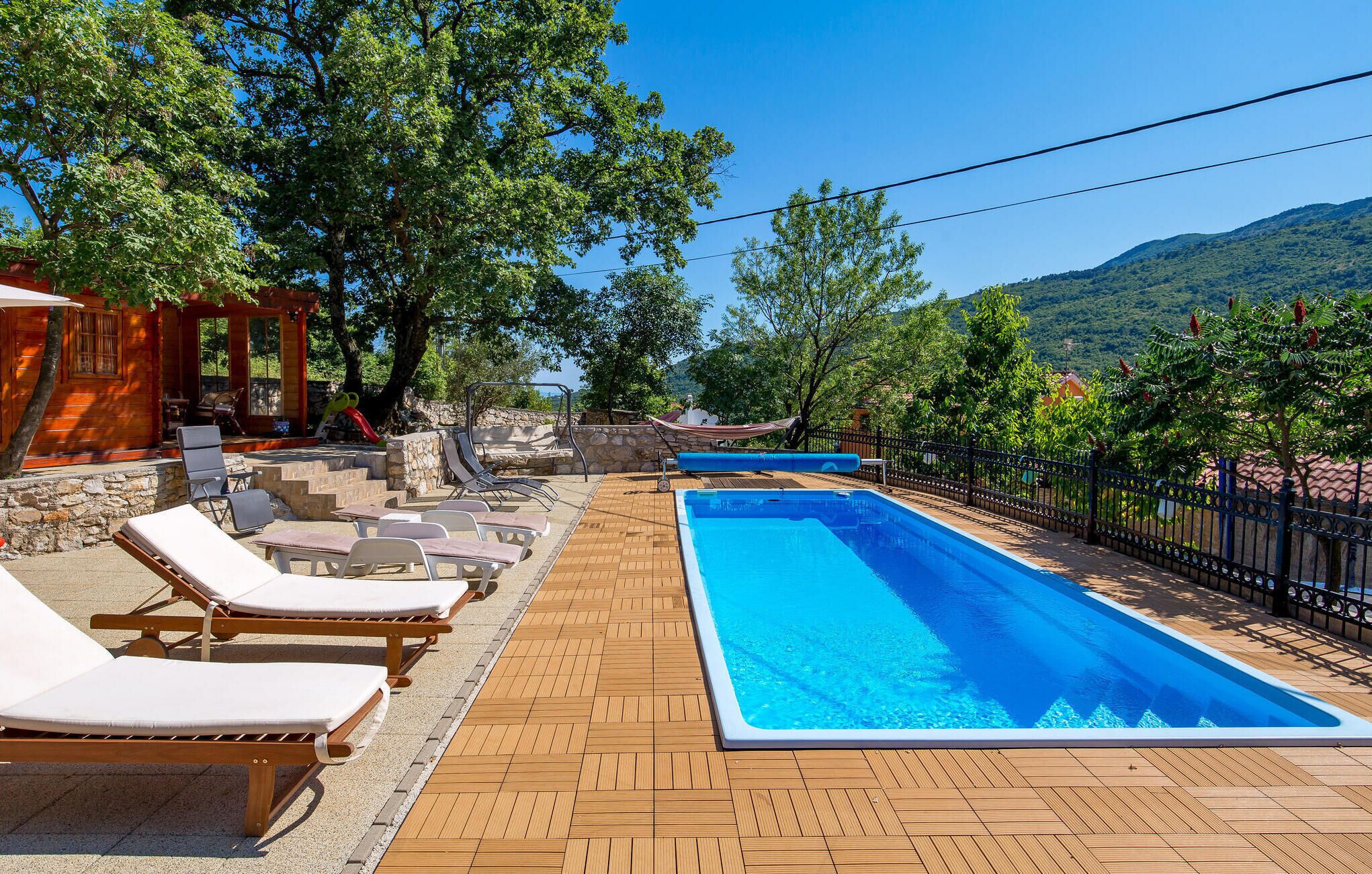 A poolside area with lounge chairs, a wooden deck, and a clear view of the surrounding landscape.
