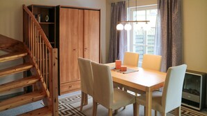 A dining area with a wooden table, four chairs, a staircase, and a wardrobe.