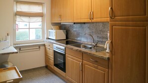 A kitchen with wooden cabinets, a microwave, a sink, and a window with a view of greenery.