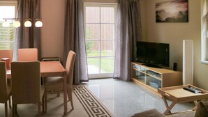 A living room with a TV, a dining table with chairs, a sofa, and a window with curtains.