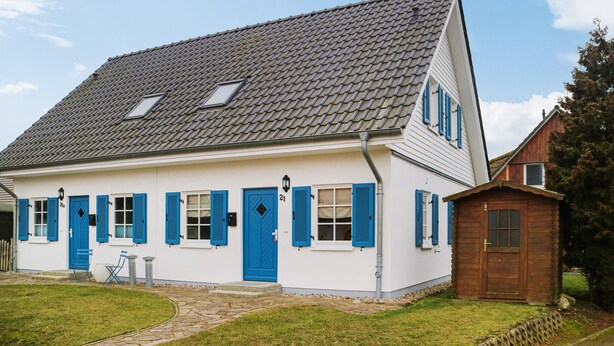 A white building with blue shutters, a stone pathway, and a small wooden structure.