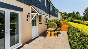 A residential building with a patio area featuring a wooden table and benches, a sliding glass door, and a well-maintained hedge. - Conveniently located to explore all that Cornwall and Devon have to offer (SALTASH)