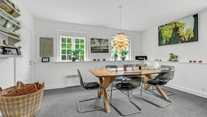 Een eetruimte met een houten tafel, zwarte stoelen, een hanglamp en een raam met beplanting buiten.