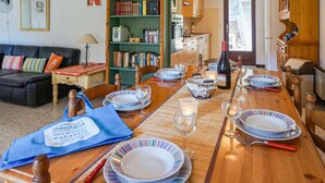 A dining area with a wooden table set for four, surrounded by chairs. A bookshelf filled with books is visible to the left. - Awesome home in Pierrerue (Pierrerue)
