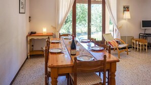A dining area with a wooden table set for four, a candle on a side table, and a view through a large window. - Awesome home in Pierrerue (Pierrerue)