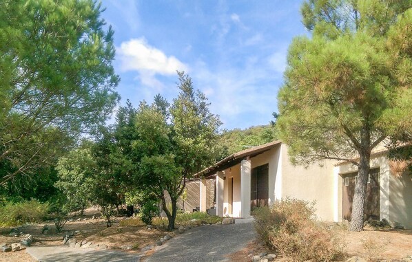 A building with a covered outdoor area, surrounded by trees and a gravel path. - Awesome home in Pierrerue (Pierrerue)