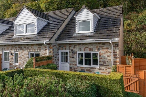 A two-story stone house with a sloped roof, dormer windows, and a well-maintained garden.