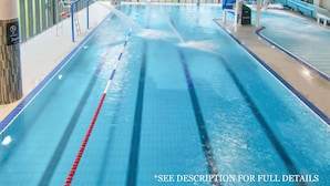 Una piscina cubierta con carriles delimitados, un cartel que indica prohibido correr y un tobogán al fondo.