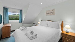 Ein Schlafzimmer mit einem großen Bett, zwei Nachttischen, einem Fenster mit Vorhängen und einem an der Wand hängenden Kunstwerk.